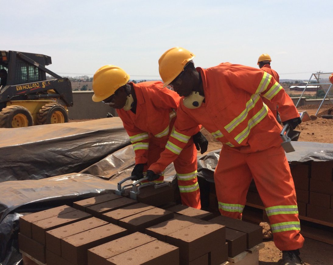 Mannen in een droog landschap aan het werk met compressed earth blocks om uiteindelijk een goed en stevig gebouw te bouwen.